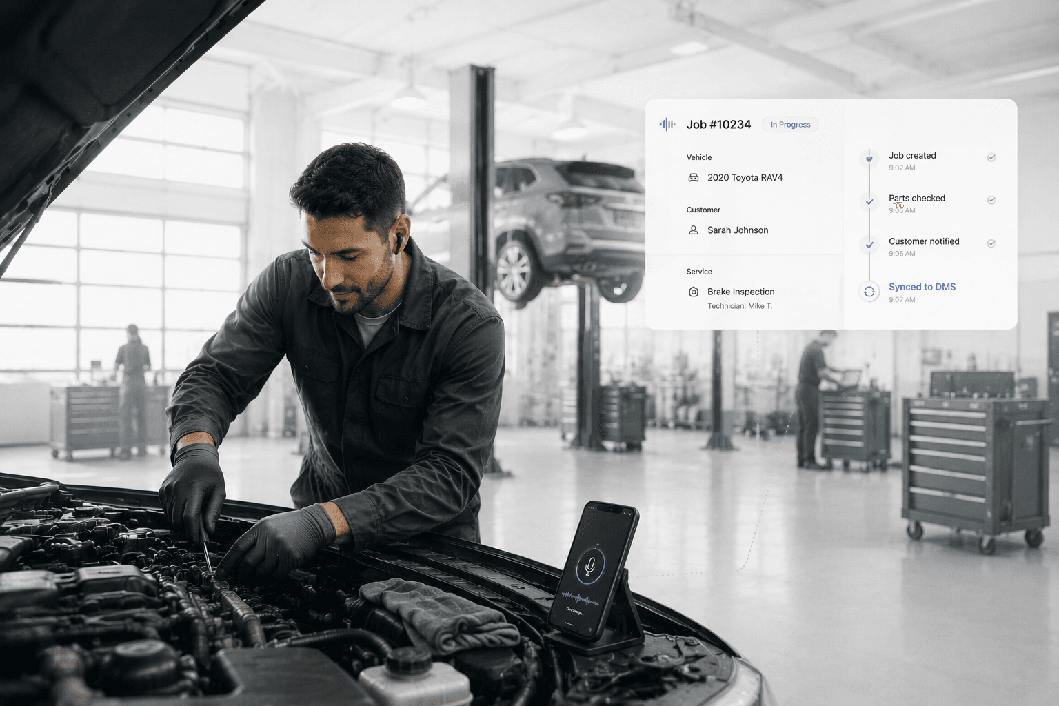 Technician working under the hood of a car with phone propped up on the engine, mic active, while a floating job card shows status syncing to the DMS